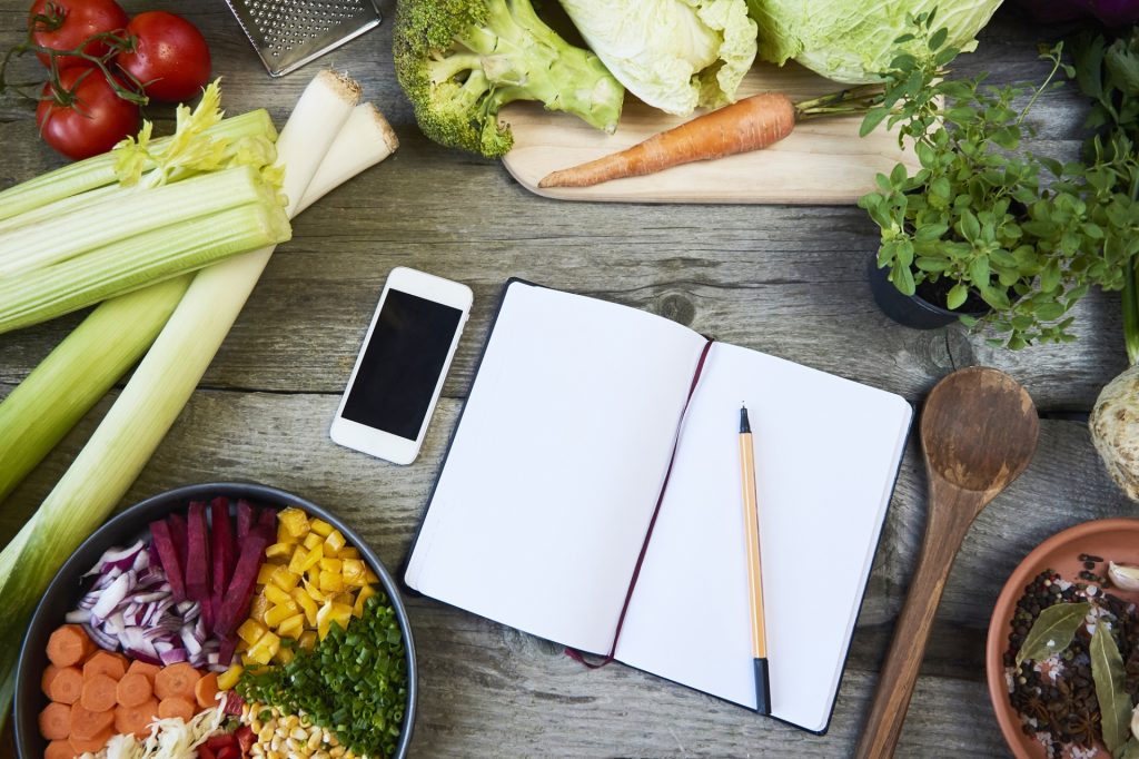 Recipe template with recipe book, spice, onion, garlic, tomatoes and greens on gray wooden background.